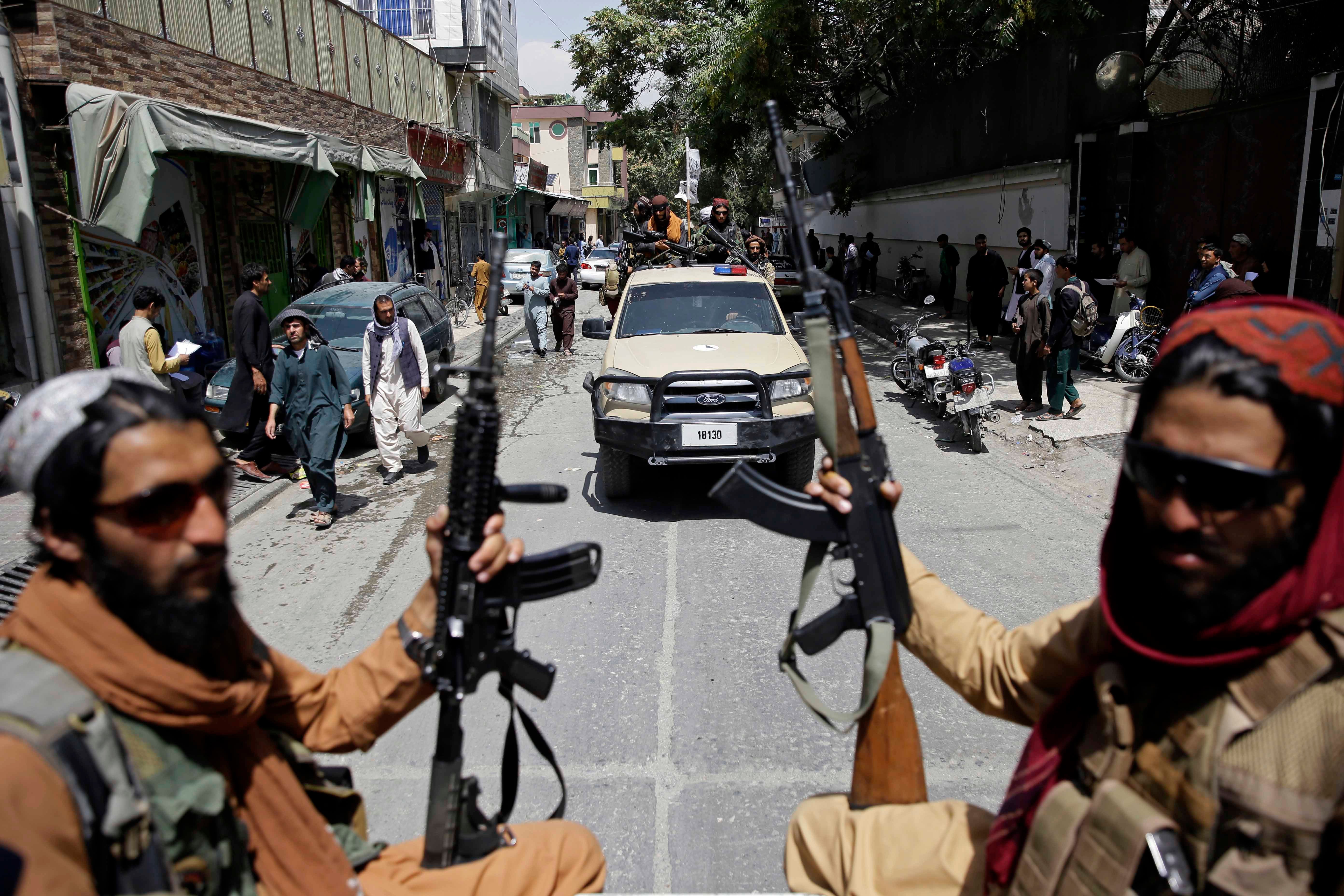 Two men hold guns while riding in the back of a truck through a city street