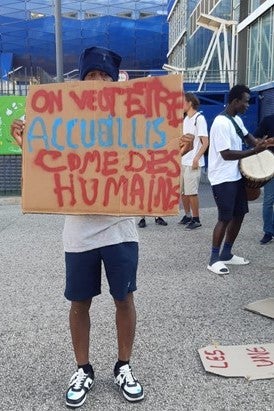 A 16-year-old Malian boy holds a sign that reads “We want to be welcomed like humans,” 