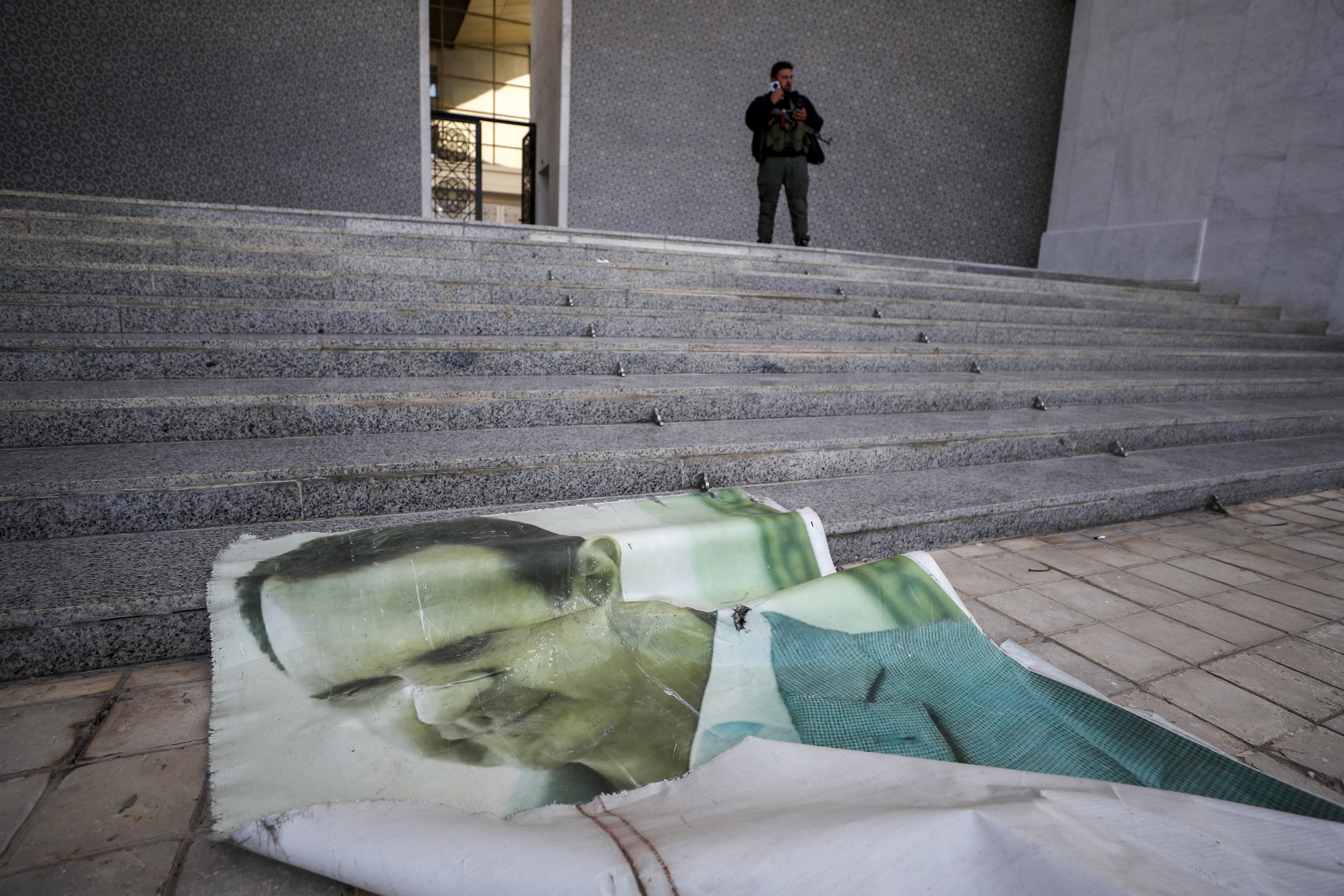 A picture of former Syrian President Bashar Assad lies on the ground as a Syrian opposition fighter stands nearby, inside the Presidential Palace in Damascus, December 8, 2024.