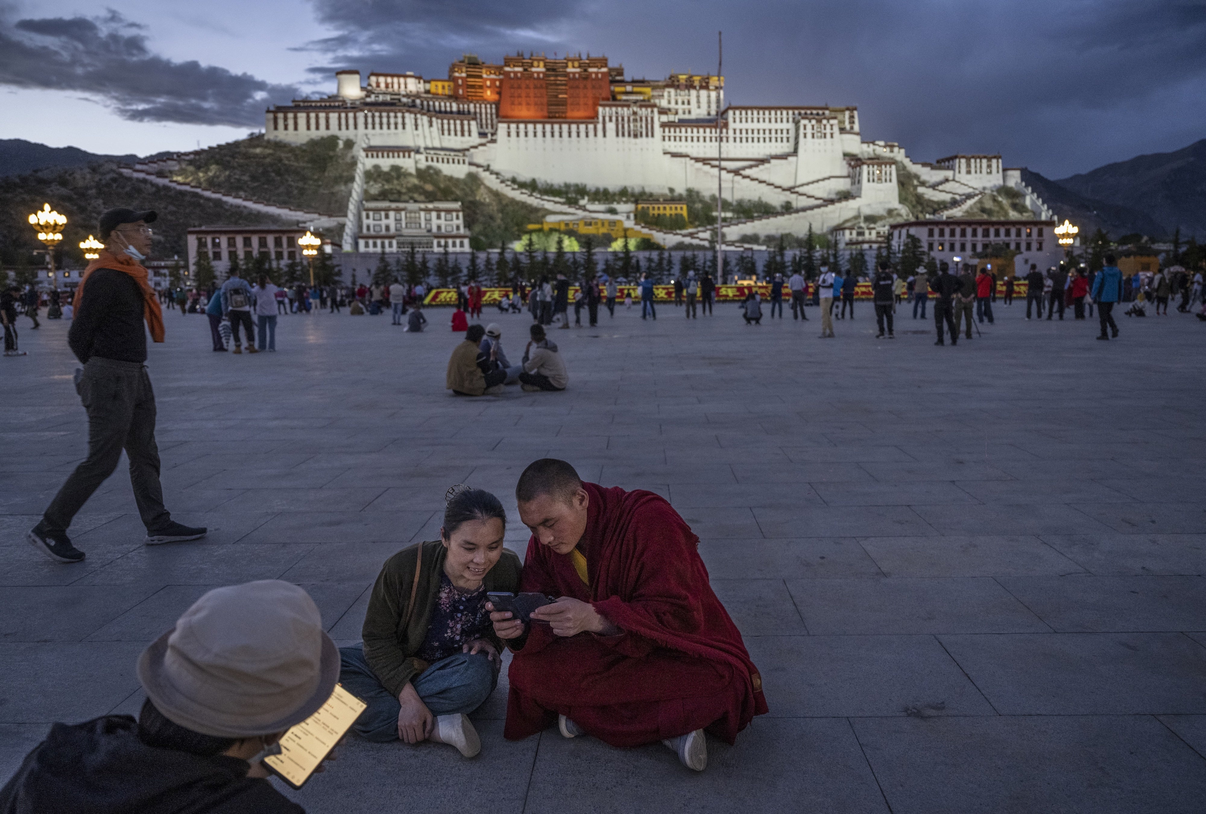 Un moine bouddhiste tibétain et une femme partagent un téléphone portable devant le palais du Potala à Lhassa, dans la région autonome du Tibet, en Chine, le 1er juin 2021.