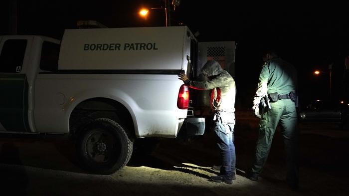 A man stands with his hands on the back of a van marked "Border Patrol"