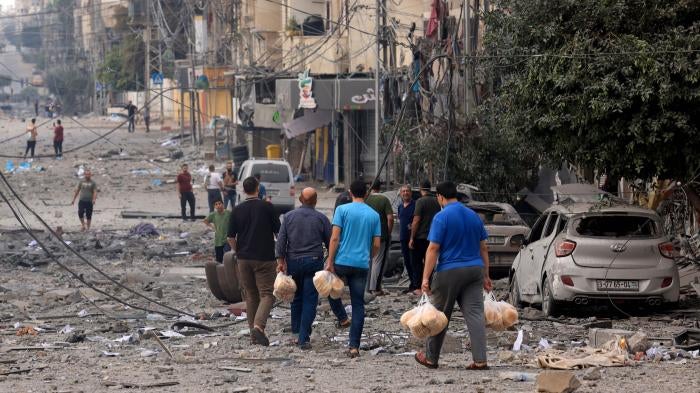  Palestinian men carry bread through a heavily bombed street following Israeli airstrikes on Gaza City on October 10, 2023.  