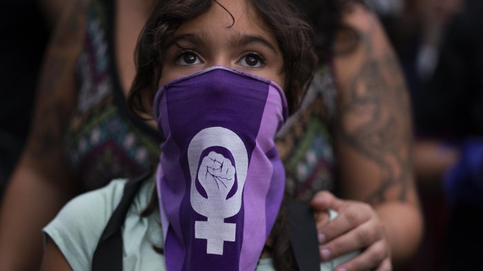 A girl wearing a purple face bandana at a march