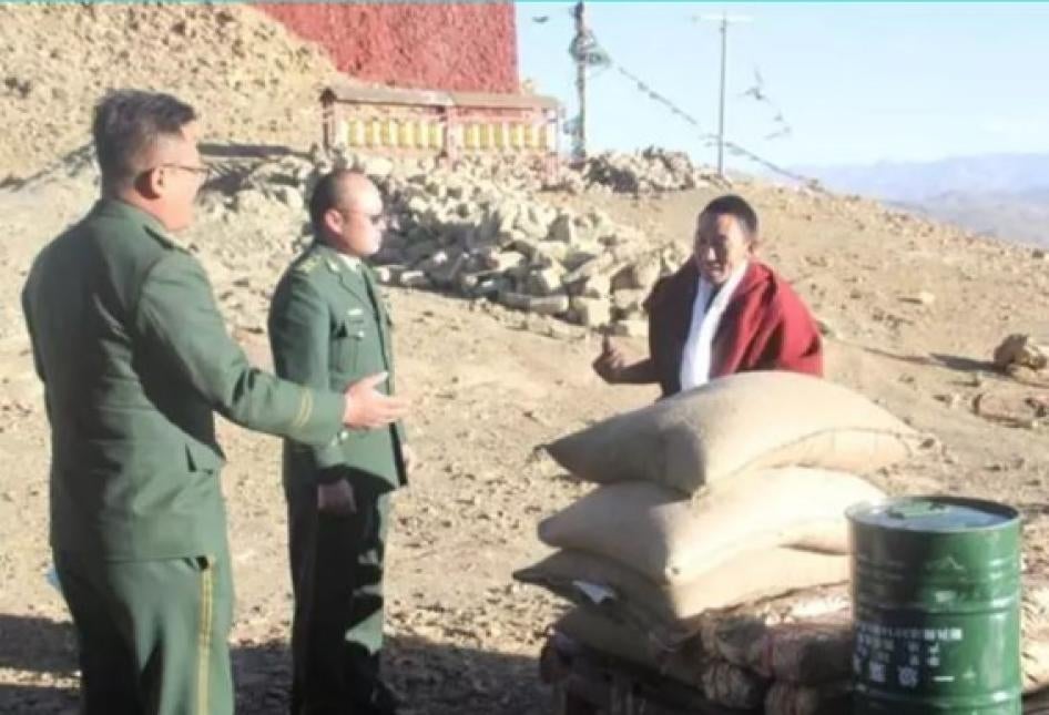Two men in official party uniforms speak to a monk
