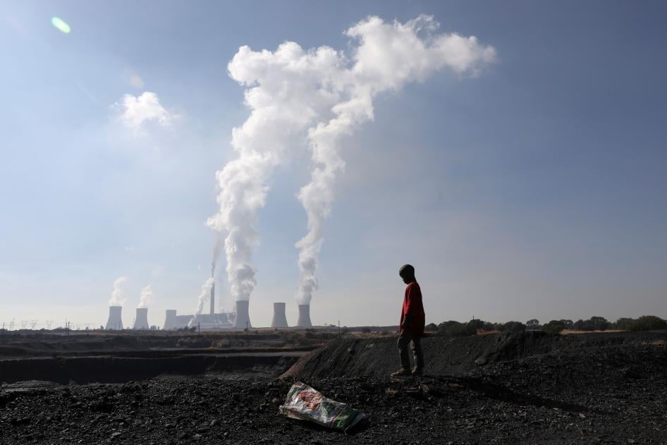 A child collects coal in front of a coal-fired power plant