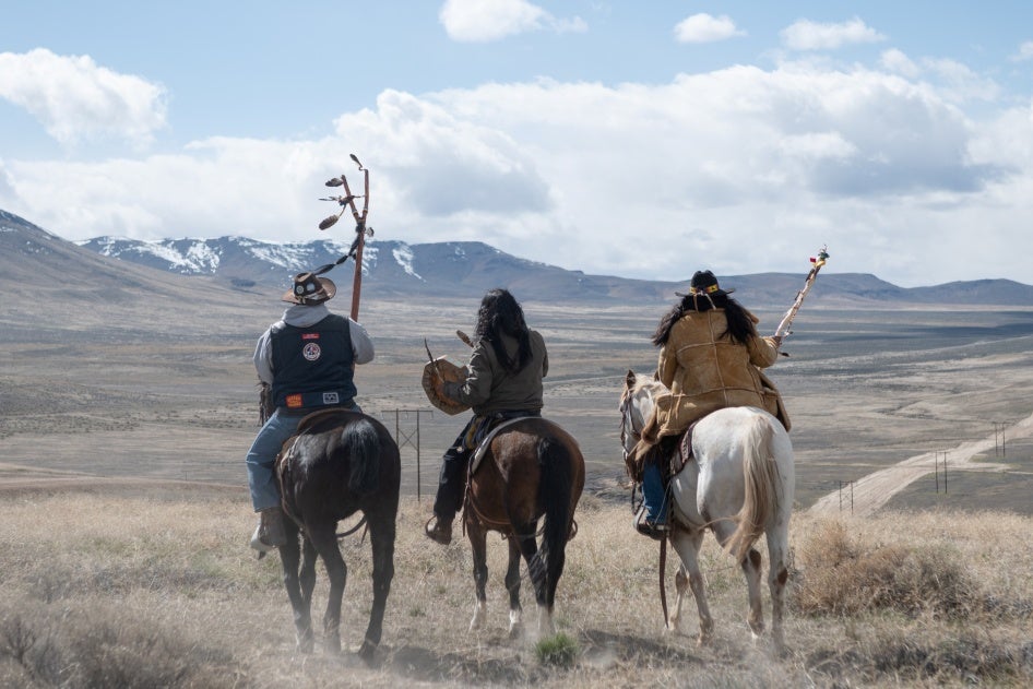 Three men sit atop horses overlooking a valley 