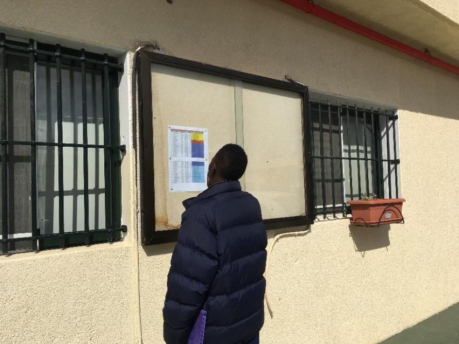 Migrantes buscan en la lista los nombres de las personas que se trasladarán de Ceuta a España peninsular, marzo de 2017.