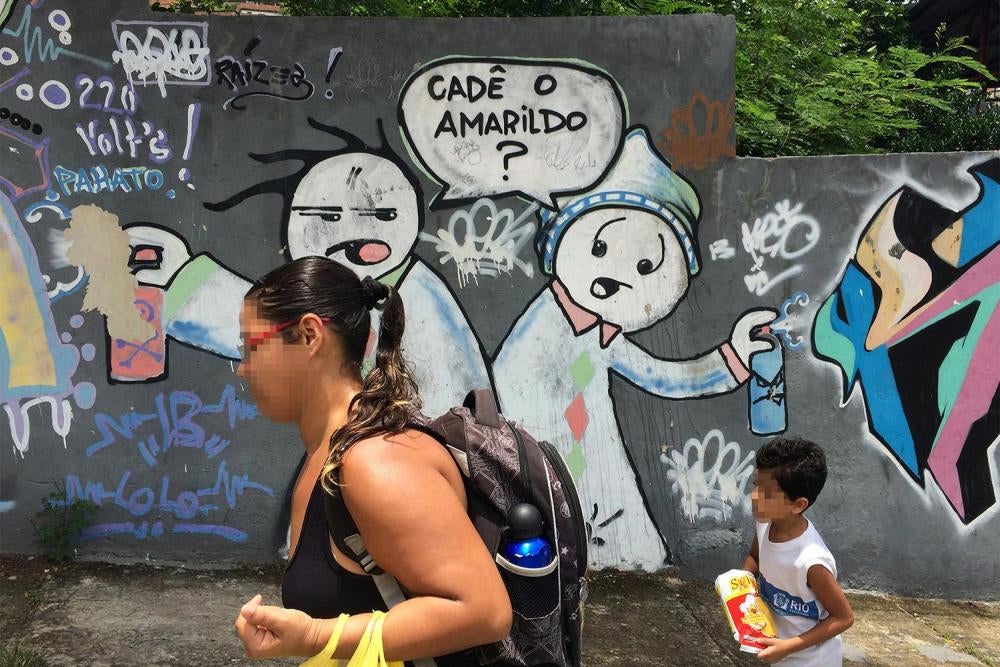 Dois moradores do Complexo do Alemão caminham em 26 de novembro de 2015 frente a um grafite que pergunta: “Cadê o Amarildo?”. O pedreiro Amarildo de Souza, de 47 anos, desapareceu após ter sido levado por policiais para a Unidade de Polícia Pacificadora (