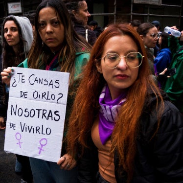 Two women hold a sign that reads “You’re tired of hearing it? We're tired of living it.”