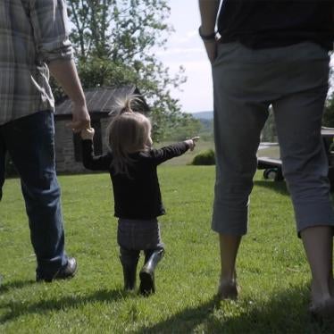 A two-and-a-half-year old born with intersex traits walks with her parents in their garden. The parents have decided to defer all medically unnecessary surgeries until their child can decide for herself.