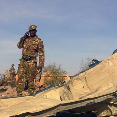 A soldier surveys the debris following a November 29, 2016 suicide car bomb attack at the Gao airport, used primarily by UN forces stationed there. The attack was claimed by the armed group Al-Mourabitoun, whose forces committed the war crime of perfidy b
