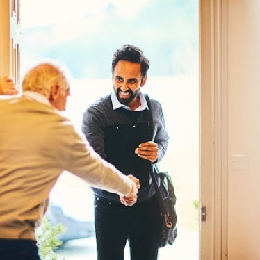 Young male community healthcare worker being welcomed by a senior man at his home. 